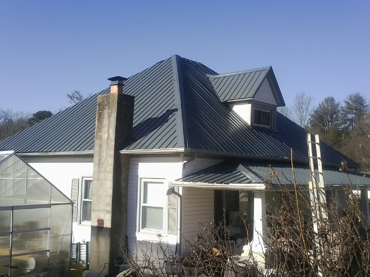 Dark blue standing seam metal roof on a white farmhouse with dormer — Slate & Tile Roof Repair by Roofing Brothers in Ogema