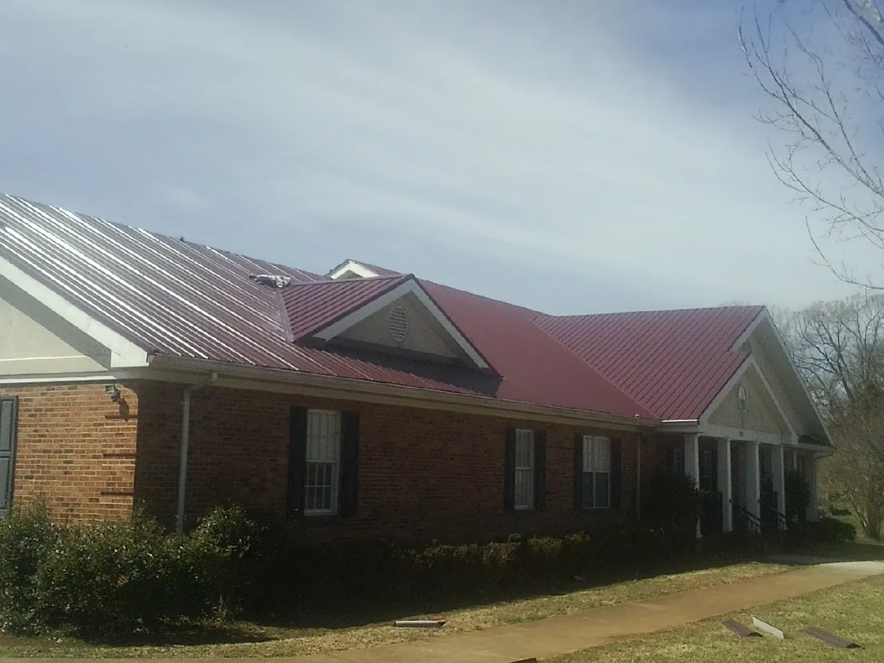 Red metal roof with gabled entries on a long brick building, from a Hail Damage Roof Repair job in Ogema