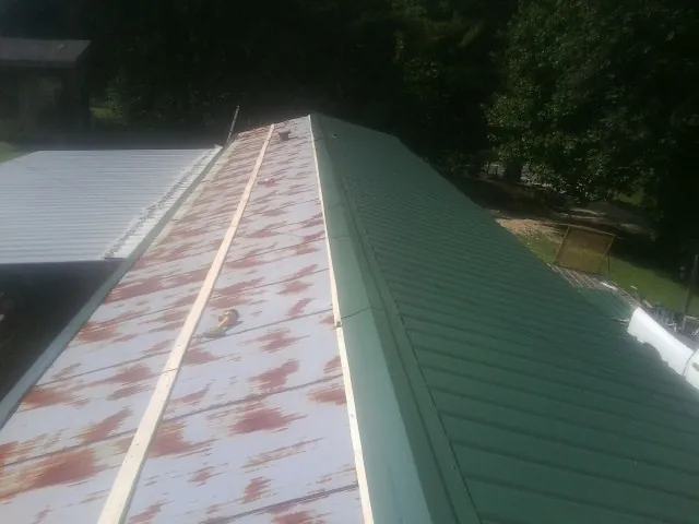 Old rusted panels beside newly installed green metal roofing — Wind Damage Roof Repair by Roofing Brothers in Ogema