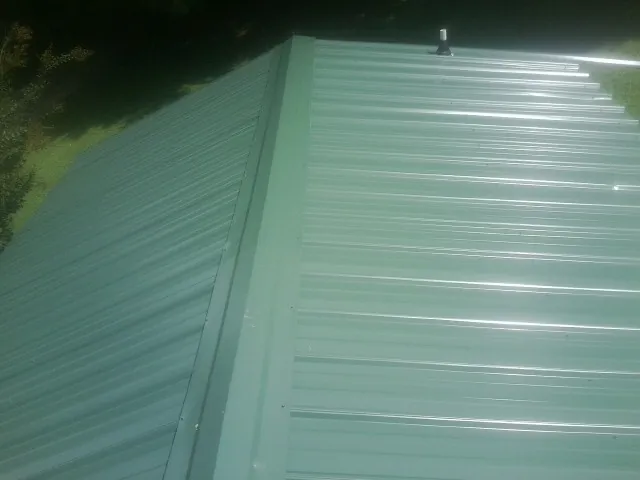 New green metal panels meeting at the ridge of a roof — Flat Roof Repair work by our crew in Ogema