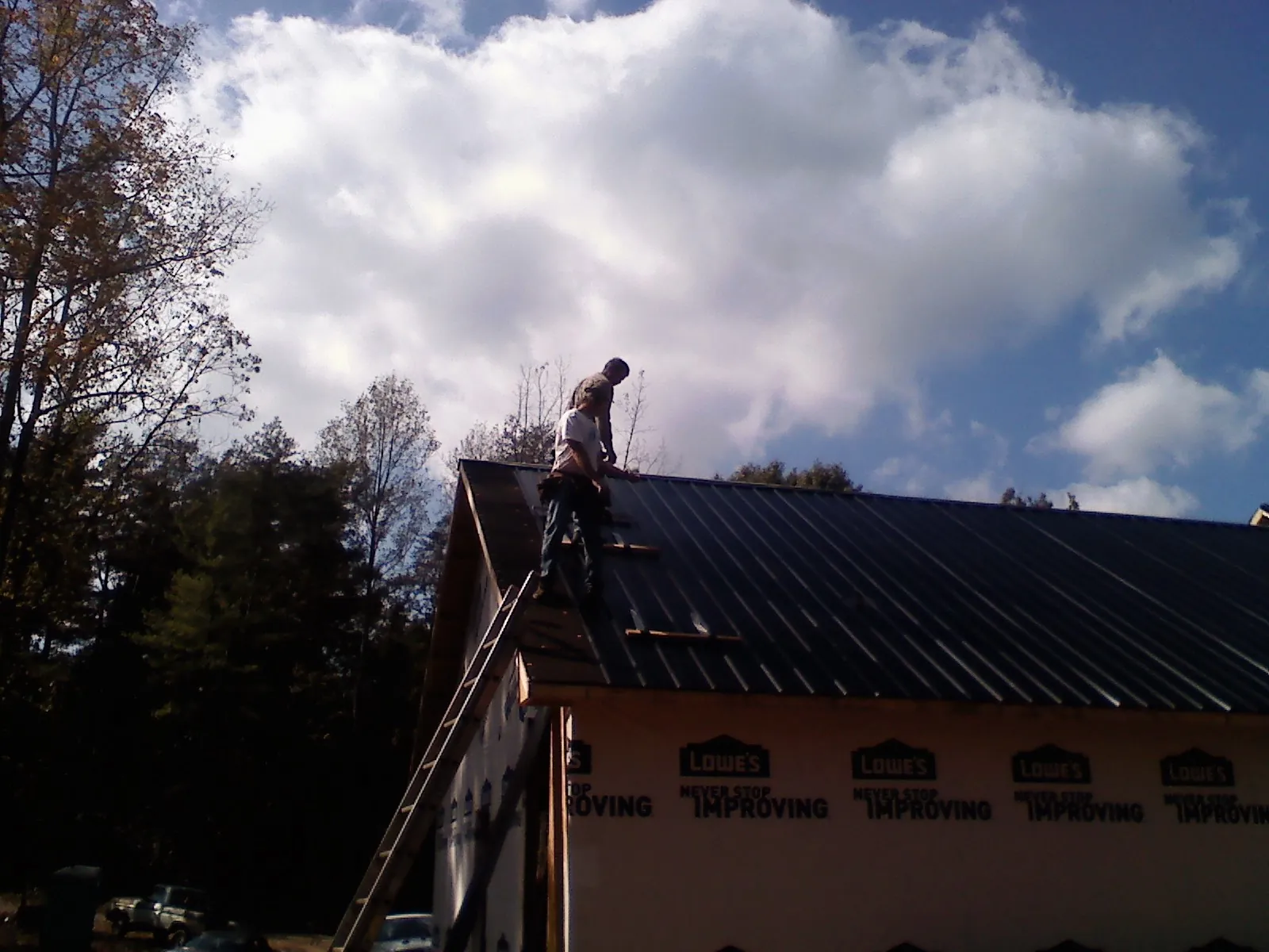 Roofer fastening dark metal panels high against a cloudy sky, from a Roof Inspection job in Ogema