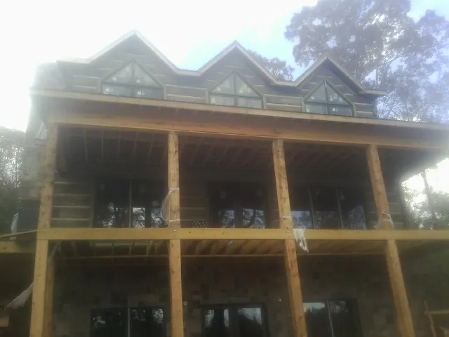 Dormers and porch framing on a large log home under construction — Roof Coating work by our crew in Ogema