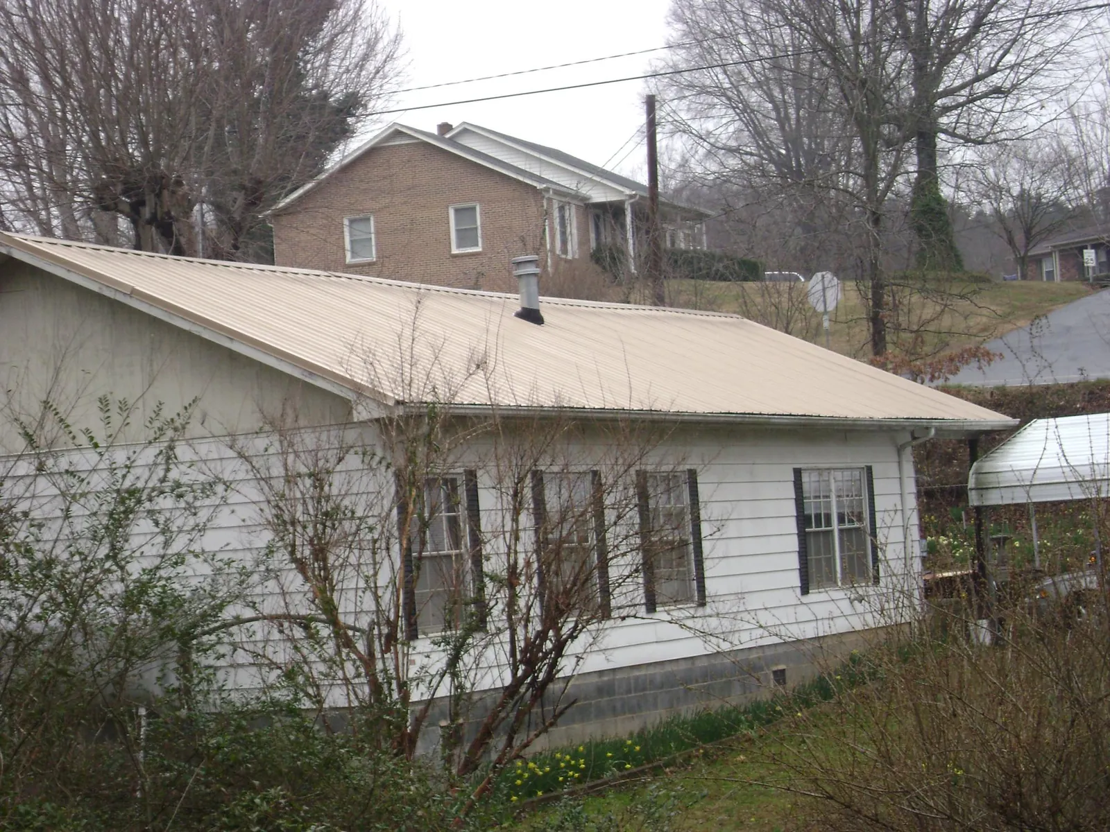 Tan metal roof on a white sided house set into a hillside — Commercial Roofing by Roofing Brothers in Ogema