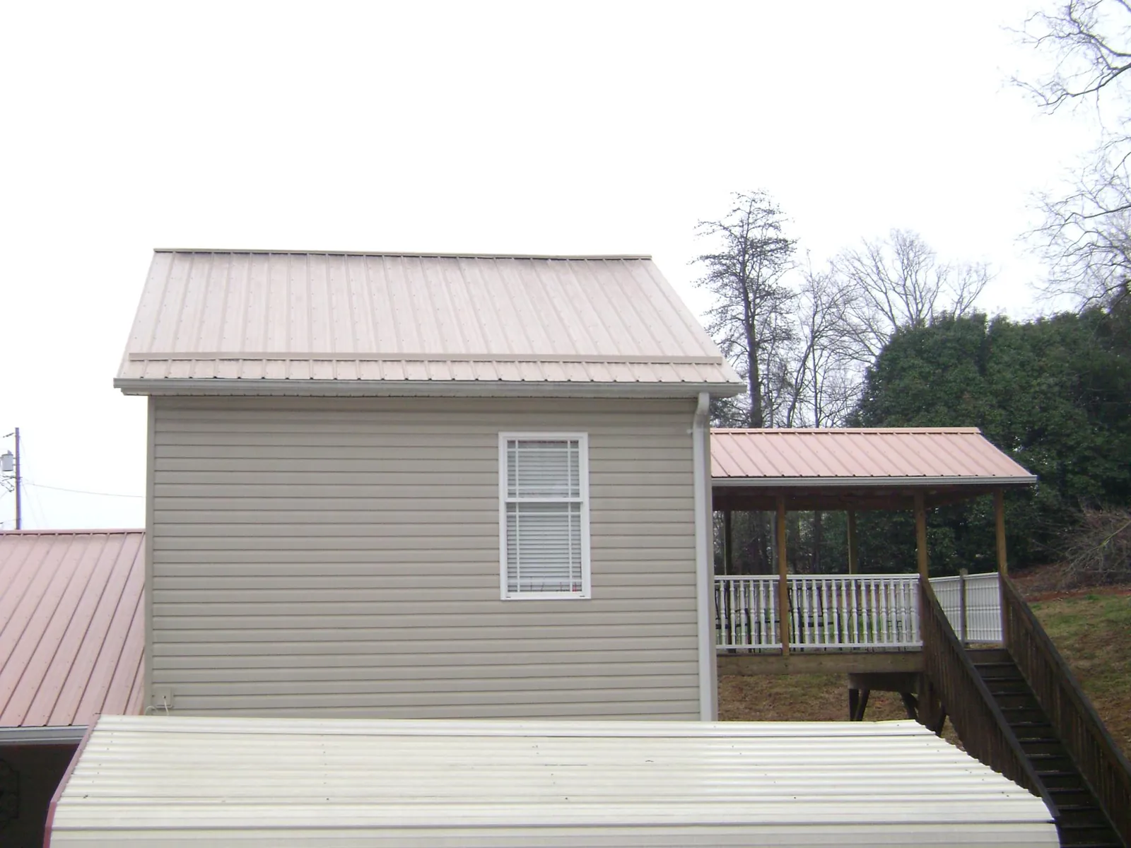 Tan metal roofs on a two story addition and attached porch, from a Roof Replacement job in Ogema